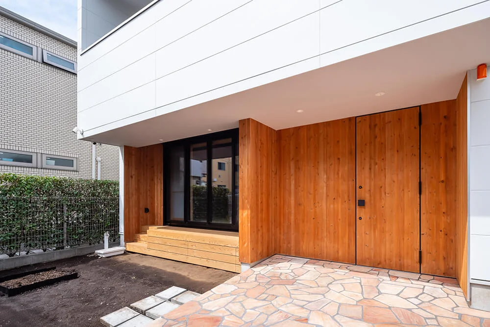 The first-floor exterior walls are clad with cedar boards, which are also applied to the steel entrance door to integrate it seamlessly with the facade.｜A Hobby-Filled Residence Featuring a Traditional Irori Hearth