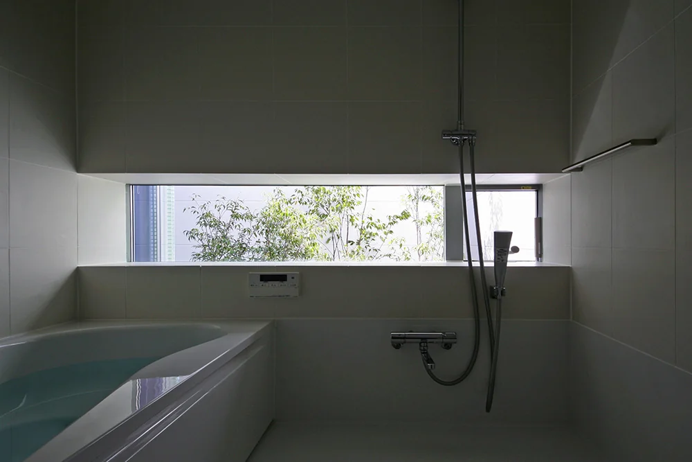 A slit-shaped bay window frames the greenery of the bath court, allowing for a relaxing bath experience.