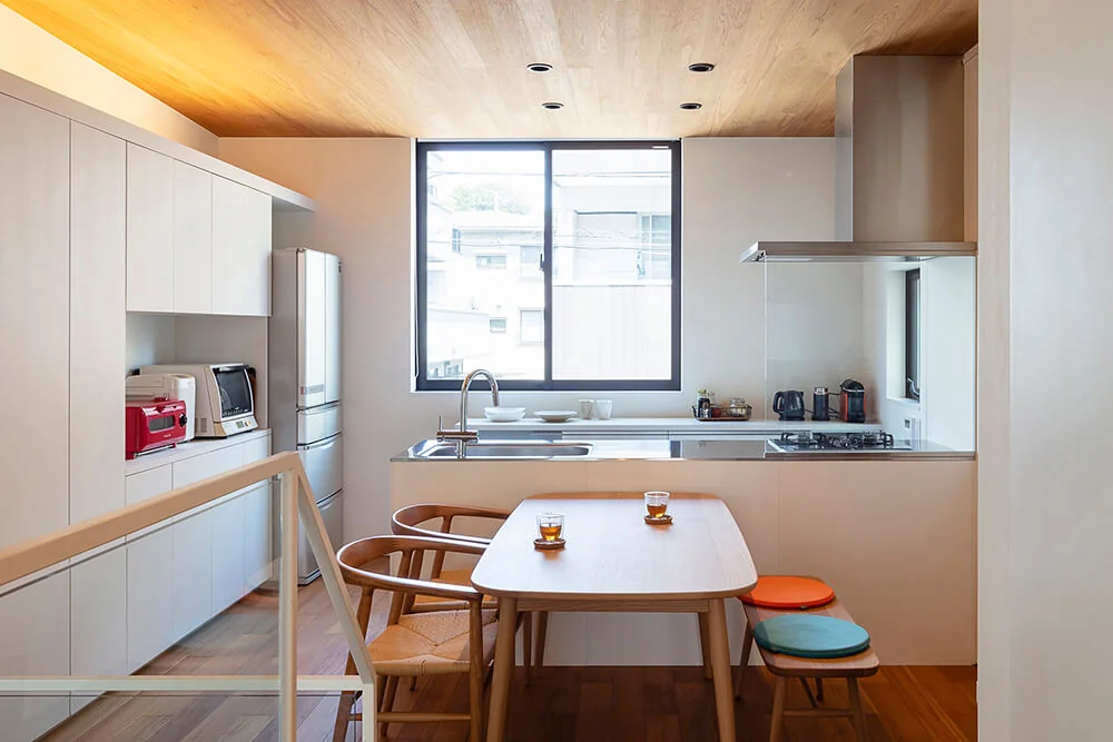 Appliance and dish storage are arranged on the kitchen’s side walls, while a large window behind the kitchen brings ample natural light.｜Two-Generation Courtyard House on a Narrow Irregular Lot