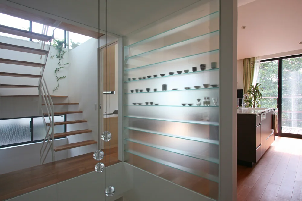 A glass shelving unit separating the LDK and atrium displays ceramics softly visible through frosted glass.