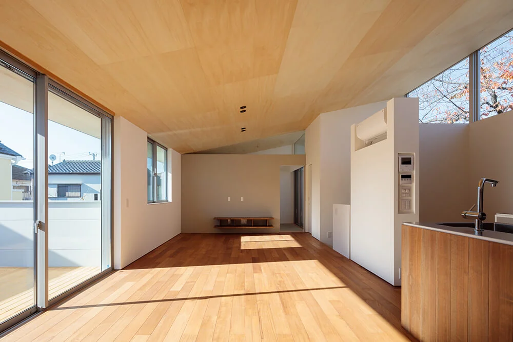 Beyond the TV counter lies a traditional Japanese-style room (washitsu), where a sloping ceiling extends deep into the space, enhancing the sense of openness.