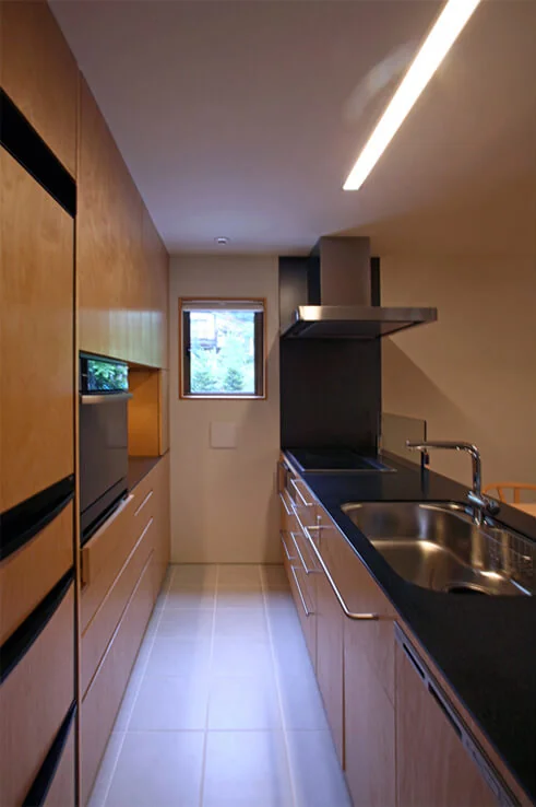 Maple veneer, matching the back storage, is applied to the refrigerator door to seamlessly integrate it｜House Nestled Among the Trees
