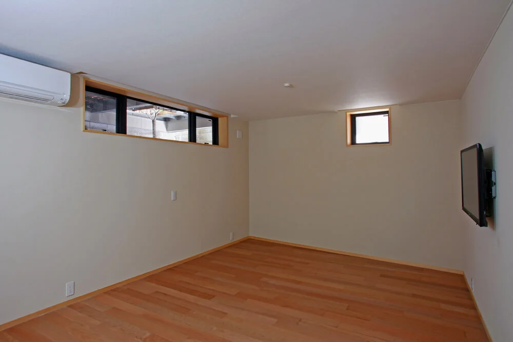 The master bedroom in the semi-basement is illuminated by high windows that draw in natural light and ventilation; walls are finished with diatomaceous earth plaster for humidity regulation.