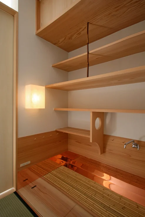 Copper sheet sink and bamboo slatted floor grate; copper sheeting extends beneath the wainscot exposed to water; a cedar board-lined charcoal storage sits between the tatami