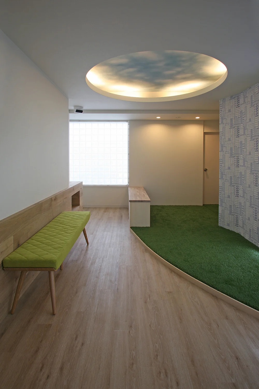 Kids’ corner floor covered with artificial turf, ceiling featuring a circular opening inspired by the sky, and wallpaper evoking an urban landscape