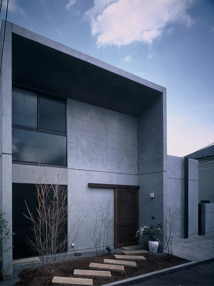 Large kura-style sliding door crafted from reclaimed wood, set within a modern exposed concrete entrance façade