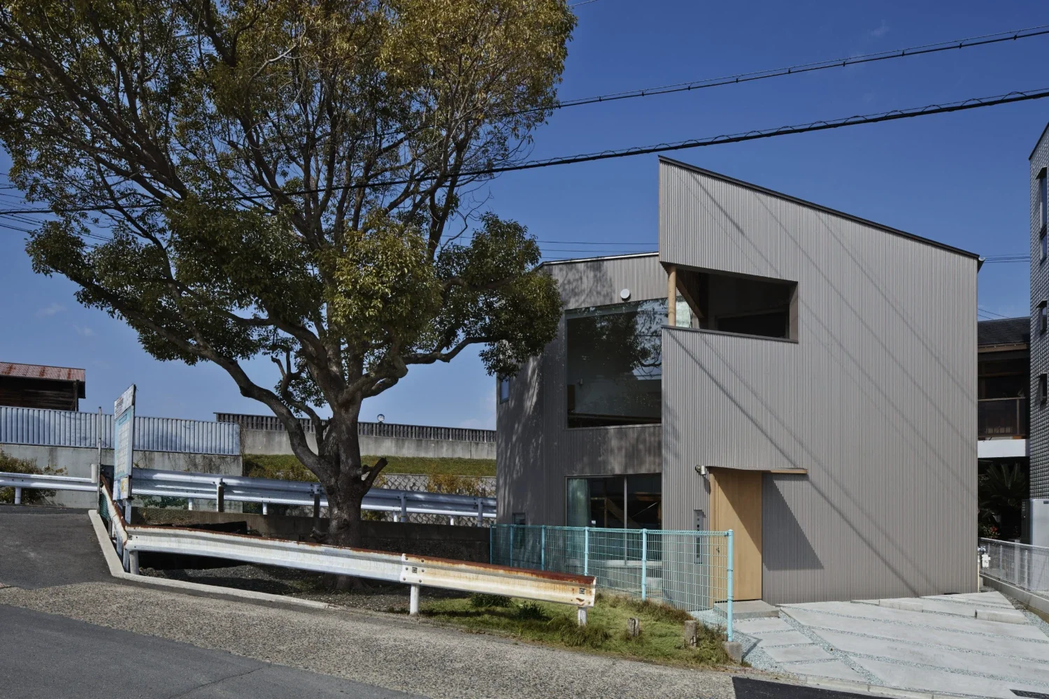 大きなクスの木のある小さな空き地に面して、三角にくぼんで開いて建つ。