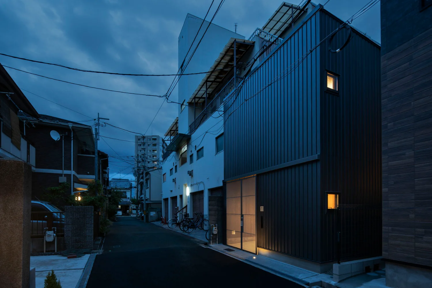 Exterior at dusk. Because suspended doors run along the façade, the entry light is specified as an uplight.